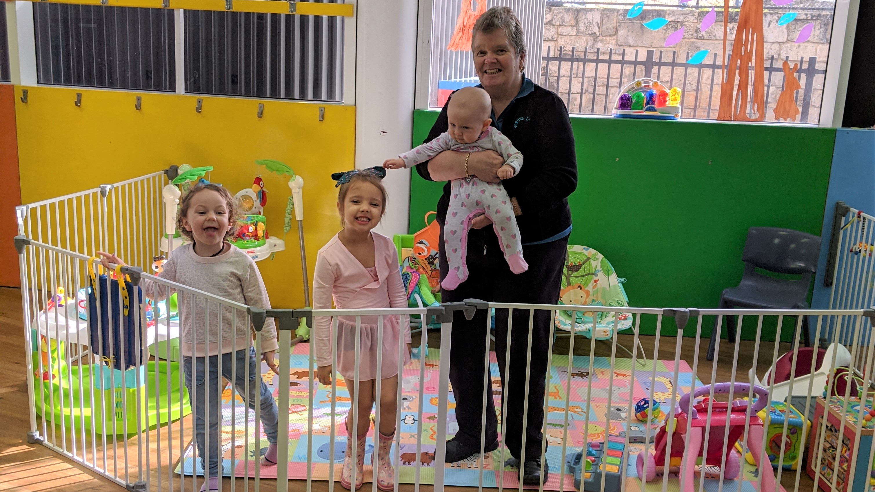 Crèche attendant holding a baby next to two happy preschoolers