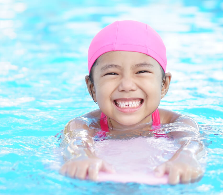 Young girl with swim cap swimming with a kickboard